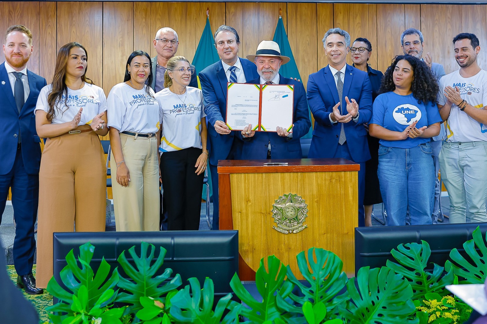 President Lula launching the Mais Professores program, standing at a podium with a Brazilian flag in the background, addressing an audience